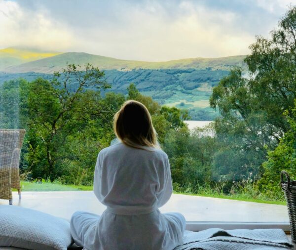 Frau meditiert in einem Bademantel mit Blick auf die Berge – Meditation auf Reisen